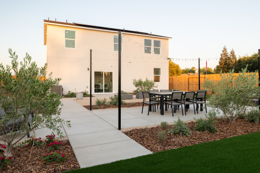 A patio with a table and chairs and a building with a fence and trees in the background.