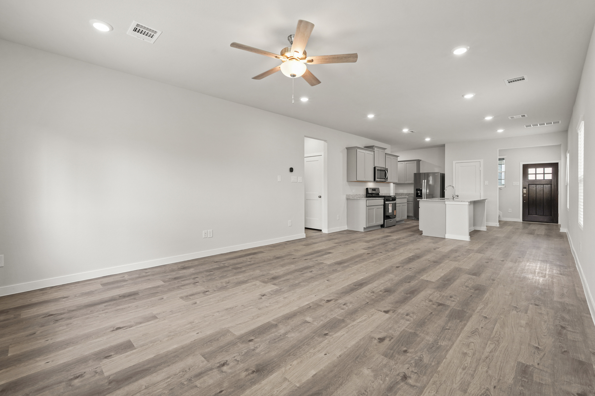 A large empty room with a ceiling fan and a wood floor.