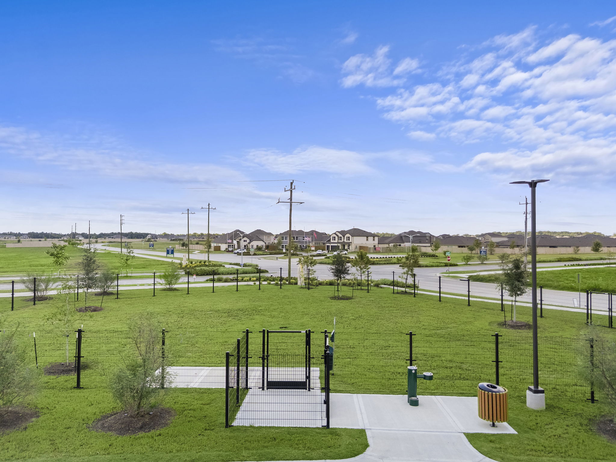 A fenced in area with a road and grass and buildings in the background.