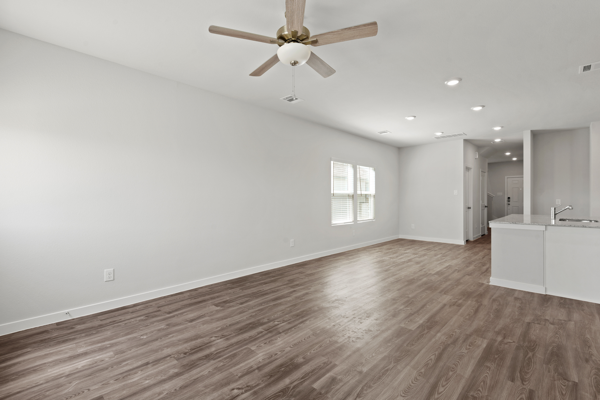 A large empty room with a ceiling fan and a wood floor.